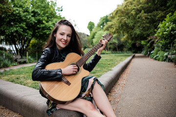 Fototapeta na wymiar Portrait of smiling young woman playing guitar in a park and looking at camera.