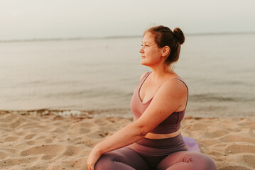 Fototapeta na wymiar Caucasian woman practicing yoga at seashore sandy beach on sunrise. Womens health and wellness. Sports body positive