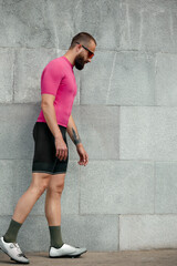 Tired sportsman in pink sportwear resting after an workout while standing against cement wall background with copy space area for text message or advertising, man runner taking break after run