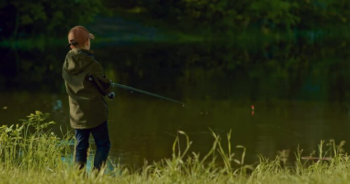 boy is fishing alone on small river shore, hooking and pulling little carp, 4K, Prores