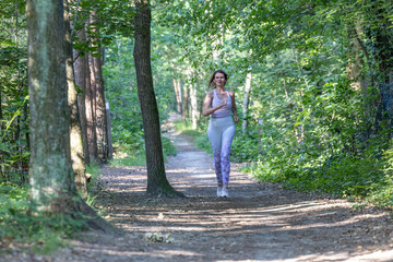 Blonde Caucasian young fitness woman running on forest trail in the sun. Exercising outdoors is healthy for active lifestyle runners. Autumn trail run woman running in nature, Outdoor jog. High