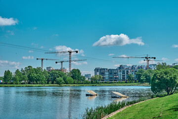 river in the city against the background of green trees and construction crane summer day