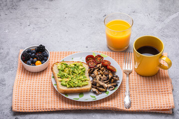 Vegan breakfast setup: avocado toast with fried tomatoes and mushrooms, berries, orange juice, and...