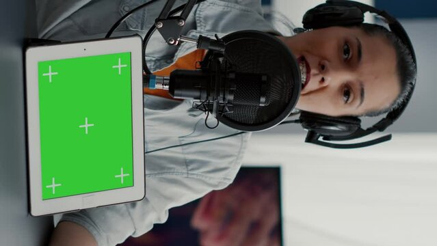 Vertical video: Influencer in studio promoting product on tablet with green screen display. Social media content creator recommending touchscreen device with chroma key with isolated background and