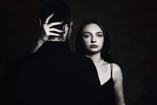 The girl hugs the guy by the neck, the guy stands with his back. Black and white portrait of a guy and a girl. loving couple