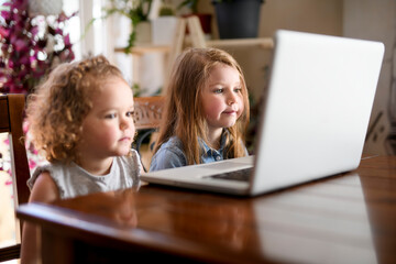 Two girls using laptop on the kitchen table