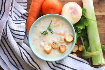 Chicken and corn soup. Chicken soup with croutons, carrots and corn. Celery, leeks, turnip, carrots, tomato in the background 