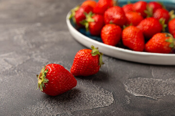 Fresh ripe strawberries in a plate on a black texture background.Vegetarian organic berry.Healthy food.Vitamins.Copy space.Place for text