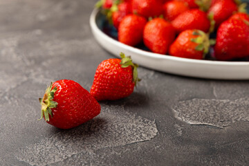 Fresh ripe strawberries in a plate on a black texture background.Vegetarian organic berry.Healthy food.Vitamins.Copy space.Place for text