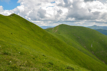 Green mountain ridge with steep slopes and high peak with a cross in the distance. Beautiful nature landscape of Carpathian Mountains, Ukraine