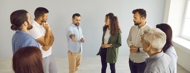 Obraz premium Group of serious people standing and talking. Modern coach meeting with business team, teaching, helping, sharing expert guidance, explaining how to find better solution and work out success strategy