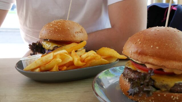 View on rench fries next to a huge cheeseburger or burger with a cutlet, lettuce, cheese and tomatoes inside. Unhealthy, fatty food on the street in a summer restaurant