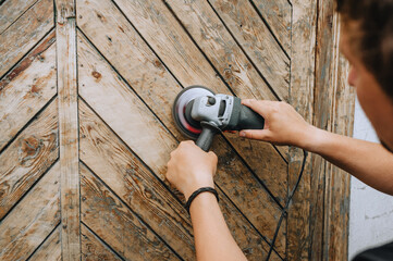 A professional man grinds a wooden door with an electric grinder. Photograph of a carpenter.