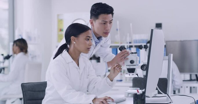 Two scientist using a computer and microscope while conducting medical research in a lab. Innovative biochemists making breakthrough and discovery in a hospital facility while using online technology