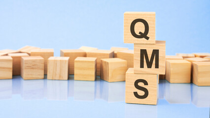 QMS. wooden cubes. blocks lie on a black background. stacks with coins. inscription on the cubes is reflected from the surface of the table. selective focus.