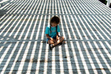 A little girl in the shade of a gazebo plays with stones. She plays of light and shadow. Childhood.