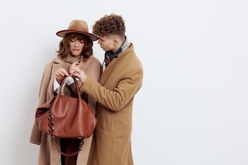 a sweet couple in love, a man and a woman in stylish autumn clothes are standing on a white background and a woman is holding a brown bag in her hand, carefully examining it together with a man