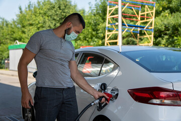 Fototapeta na wymiar A young man pours gasoline into the gas tank of a white car.A young man pumps gasoline into a gas tank. Fuel and oil crisis. The concept of gasoline prices and the oil crisis.