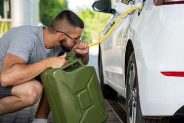 A young man steals gasoline from the gas tank in the white car. A young man pumps gasoline from a...