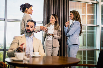 Coffee break at the office, two male colleagues talking and three young females drinking coffee