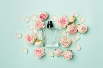 Bottle of perfume with rose flowers on color background, top view