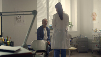 Woman doctor conducting health examination senior patient in hospital office. 