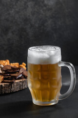 frothy cold beer is poured into a glass large glass, on a wooden substrate in an assortment of beer snacks, fried crackers, pistachios