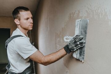 Builder in work overalls plastering a wall indoor