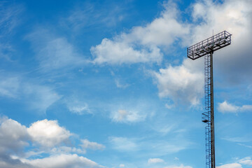 Naklejka premium Metal high tower with lanterns in the stadium, sports lighting, spotlight against the blue sky