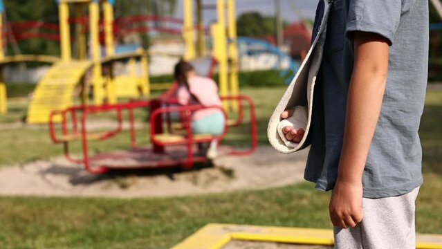 a child's arm is broken. cropped photo of boy with a fractured limb outdoors on the playground. children play on background. fracture injury in the summer holiday. kid with plaster cast on the arm