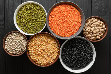 Overhead view of bowls of assorted raw legumes on a dark wooden table