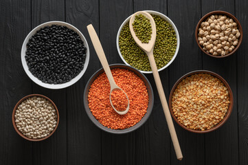 Overhead view of bowls of assorted raw legumes on a dark wooden table