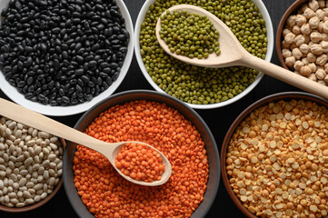 Overhead view of bowls of assorted raw legumes on a dark wooden table