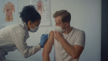 African nurse injecting vaccine in man shoulder. Doctor vaccinating patient.