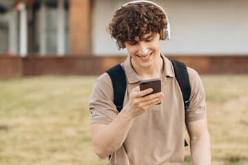 Attractive curly young man university or college student with phone walking around campus