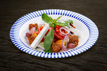 Greek salad with feta cheese and aromatic herbs. On a dark background, isolated. Vegetarian dish.