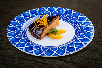 Orange, sponge cake under chocolate frosting. On a dark background, isolated.