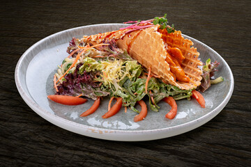 Salad with sweet and sour chicken in a waffle cone on a bed of lettuce leaves. On a dark background, isolated.