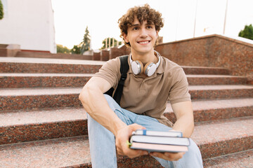 Obraz premium Attractive male student sits on the steps of the university and reads something, preparing for exams