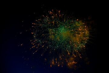 Bright fireworks with a green center with orange sparks flying towards the background of the night sky. High quality photo