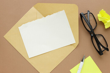Greeting, congratulations or notification layout. A blank sheet of paper on a brown envelope, black glasses yellow stickers on a clean table. Table top view, flat lay, copy space.