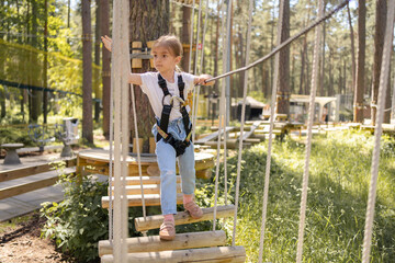 Beautiful little child climbing and having fun in adventure park. Children summer activities. Child climbing on rope park. 