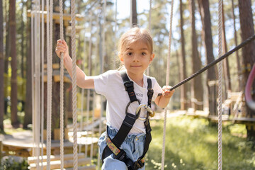 Beautiful little child climbing and having fun in adventure park. Children summer activities. Child climbing on rope park. 