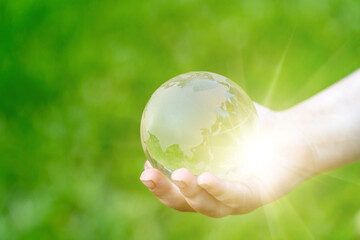 Glass globe in girl hand on blurred green grass banner background with sunlight in city. Concept of...
