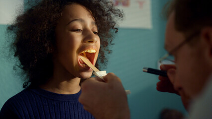Doctor using depressor checking girl throat closeup. Medic looking in open mouth