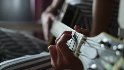 Close-up cropped shot of unrecognizable little girl learning to play guitar using electric guitar for music self studying at home. Closeup hands of small kid playing chords on guitar in bedroom.