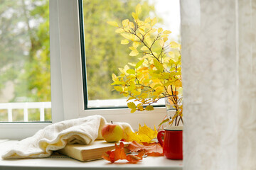 Autumn still life on the window. A book, a scarf, a mug of tea and an apple