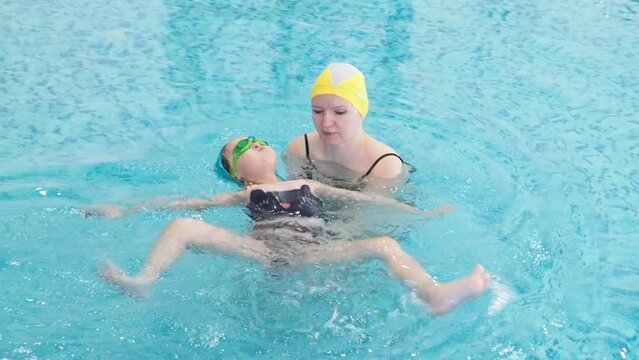 Little girl learning to swim with mother in big sport pool. Swimming school for small children. Healthy kid enjoying active lifestyle. Preschooler practicing with foam pad and noodle.