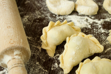 Ukrainian dumpling with cherries in the center of the frame. Nearby is a rolling pin, dough blanks for dumplings