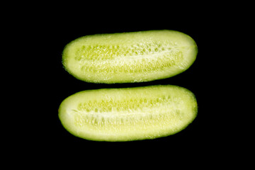 A cucumber, cut into two halves, is lying on a black background